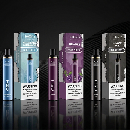 HQD Plus disposable vapes and packaging in Blueberry Lemonade, Grapey, and Black Ice on a dark studio background.